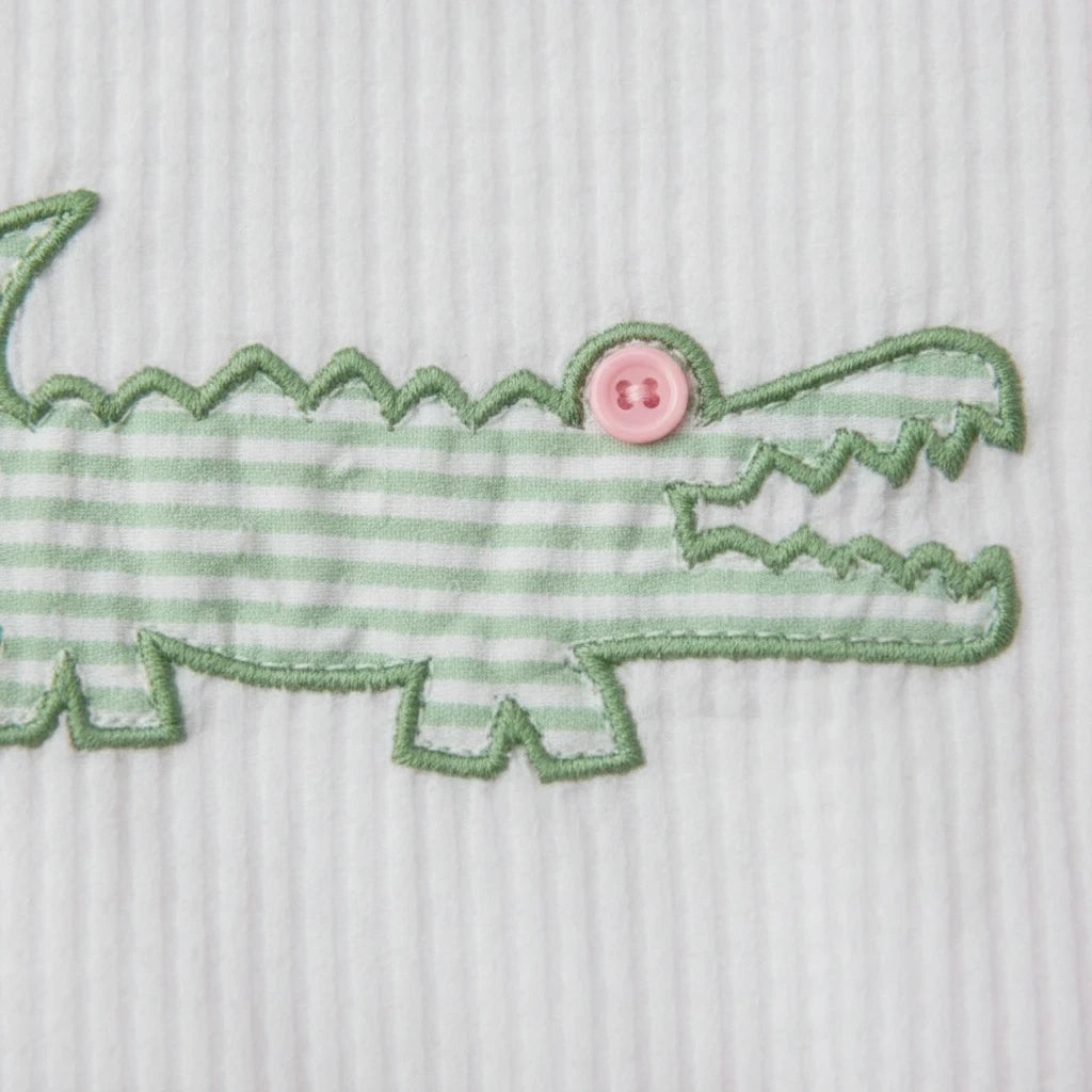 Sea Dragon Dreams pink seersucker baby romper featuring a green striped alligator appliqué with a pink button eye.