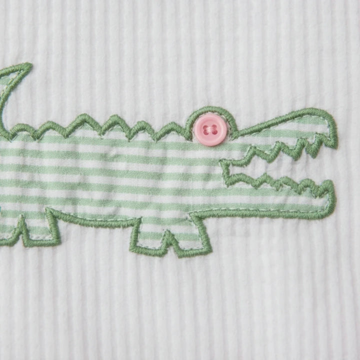 Sea Dragon Dreams pink seersucker baby romper featuring a green striped alligator appliqué with a pink button eye.