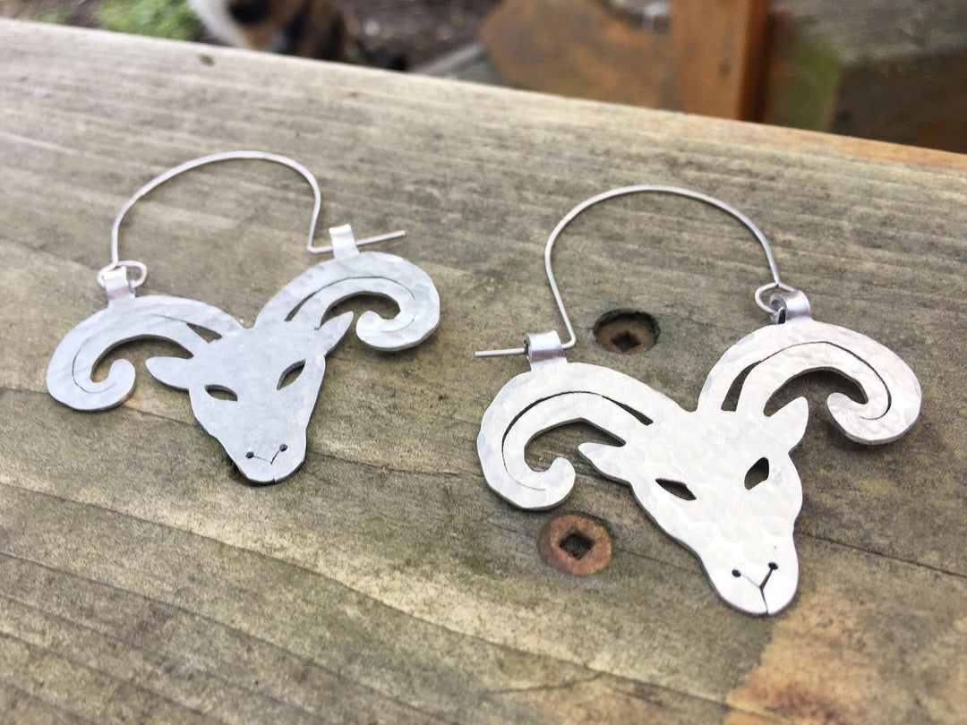 Sea Dragon Dreams handmade aluminum Aries ram hoop earrings with stainless steel ear wires on a wooden surface.