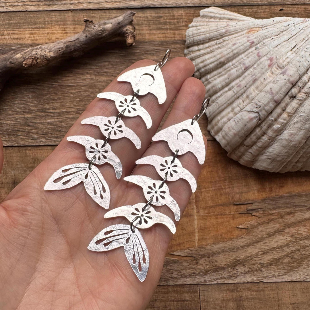 Sea Dragon Dreams handmade aluminum fish bone earrings with flower and crescent moon cutouts held in a hand.
