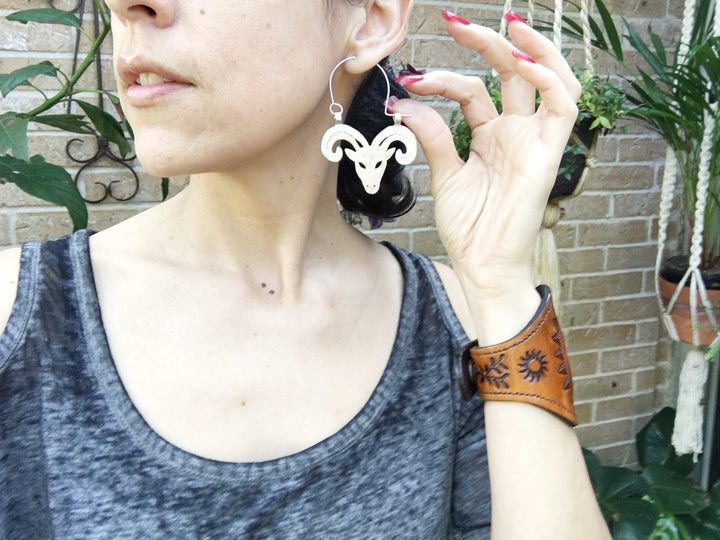 Sea Dragon Dreams handmade Aries ram hoop earrings in silver-tone aluminum worn by a woman with a leather cuff.
