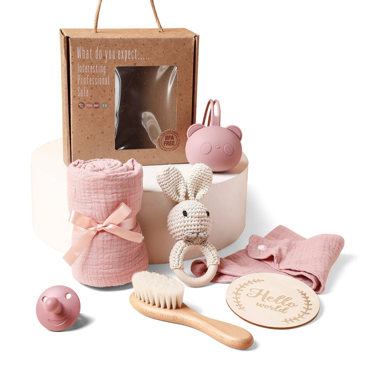 Sea Dragon Dreams baby gift set featuring a pink muslin swaddle, bunny rattle, wooden brush, and pacifier in a box.