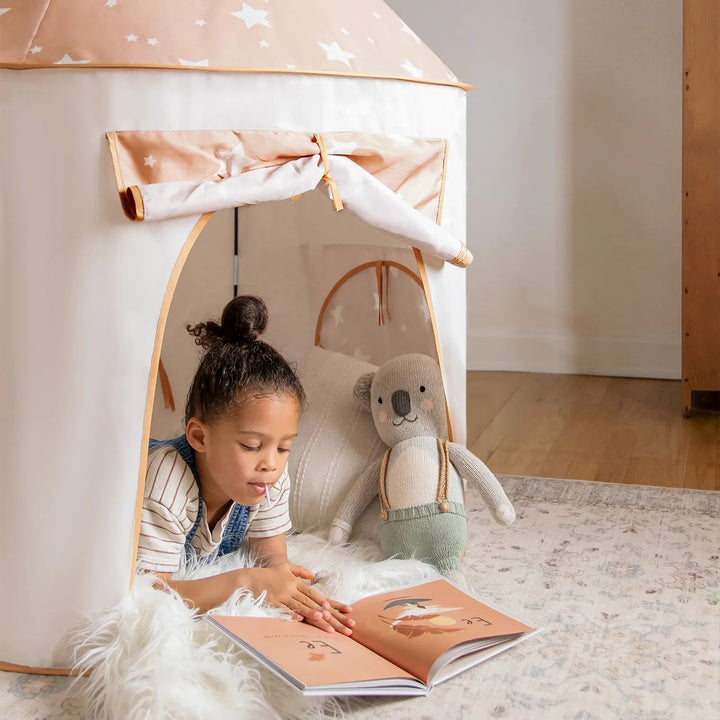 A child reading inside a beige Sea Dragon Dreams 3-in-1 play tent with star patterns and a plush koala toy.