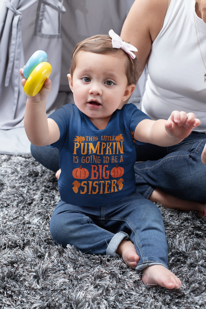 Sea Dragon Dreams infant navy blue cotton t-shirt with Big Sister Pumpkin graphic, worn by a baby on a grey rug.