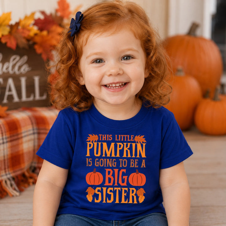 Sea Dragon Dreams infant blue cotton t-shirt with Big Sister Pumpkin graphic, worn by a smiling toddler in autumn.