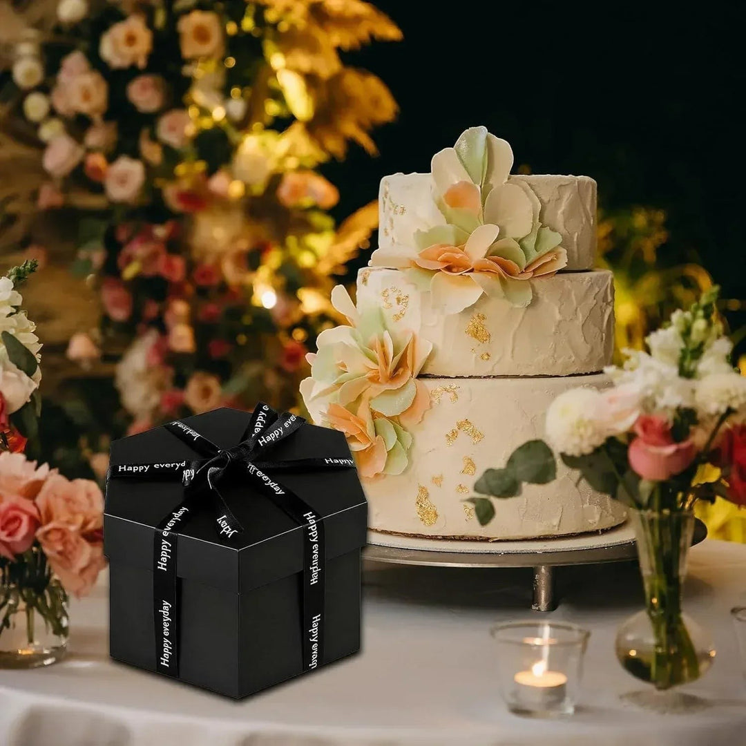 Sea Dragon Dreams black hexagonal explosion photo gift box tied with a ribbon, displayed next to a wedding cake.