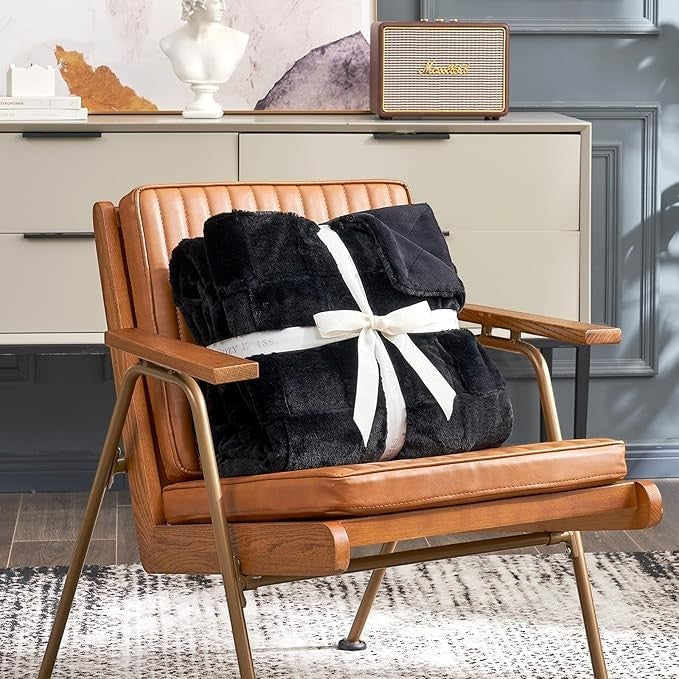 Sea Dragon Dreams black checkered faux rabbit fur queen blanket tied with a white ribbon on a leather chair.