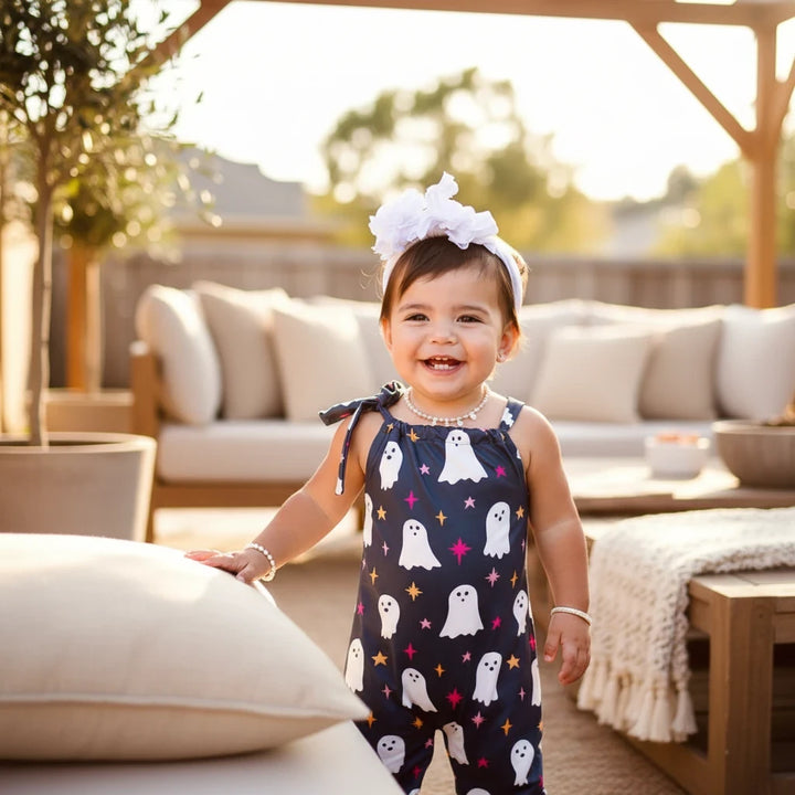 A toddler girl wearing a Sea Dragon Dreams black jumpsuit with a white ghost and sparkle pattern and adjustable straps.
