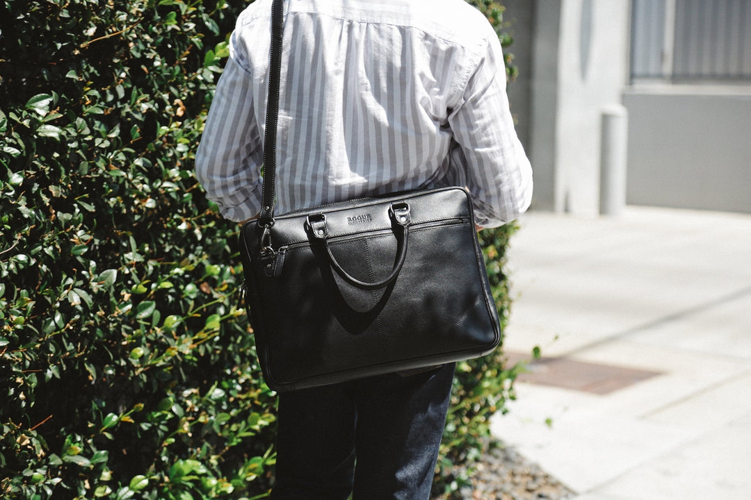 Sea Dragon Dreams black leather slim laptop bag worn over the shoulder by a person in a striped shirt outdoors