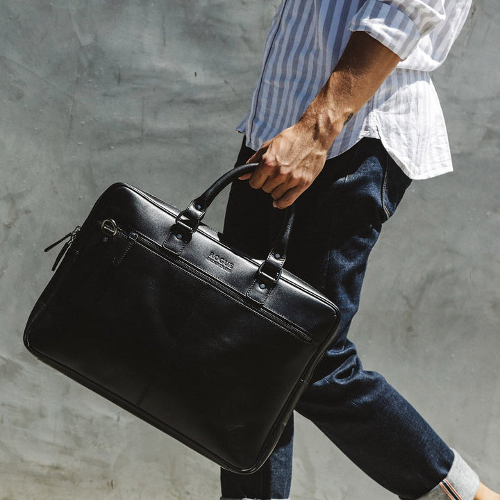 Sea Dragon Dreams black leather slim laptop bag with nickel hardware held by a man in a striped shirt and jeans