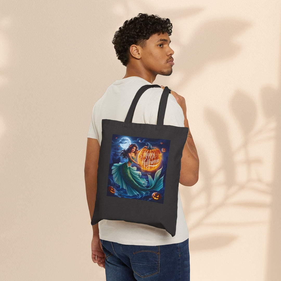 Sea Dragon Dreams black cotton canvas tote bag with a mermaid Halloween graphic worn over the shoulder by a man.
