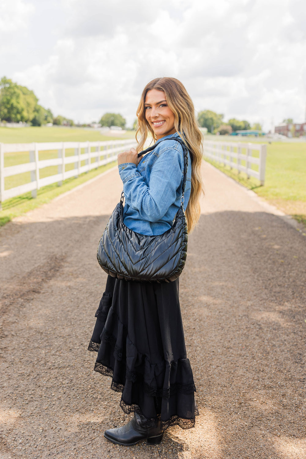 A woman wearing a Sea Dragon Dreams black nylon HydroHobo crossbody bag with a half-moon shape on a country road.