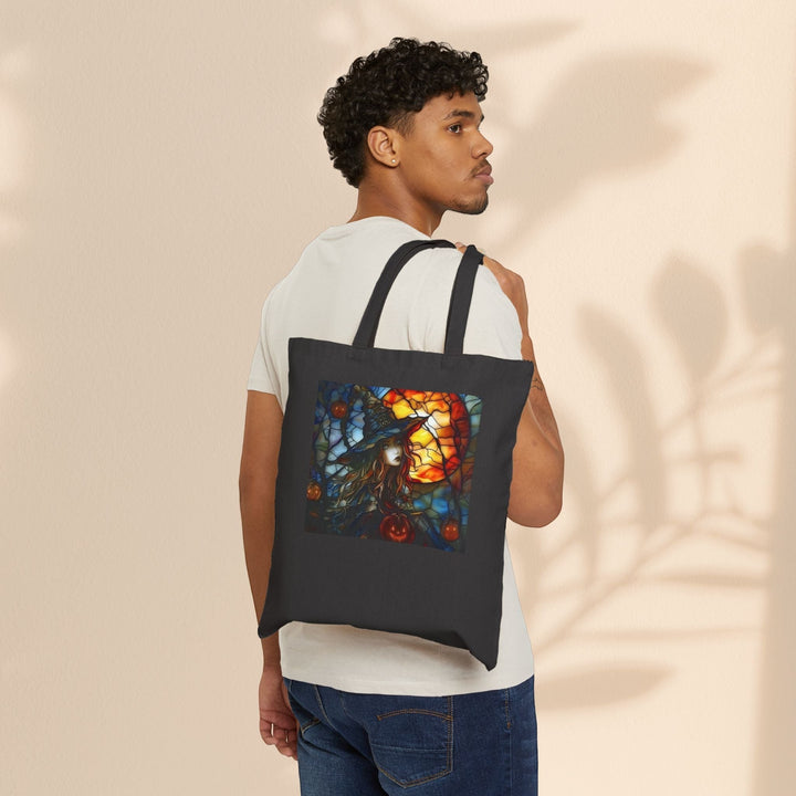 A man wearing a Sea Dragon Dreams black cotton canvas tote bag with a witchy Halloween stained glass design on his shoulder