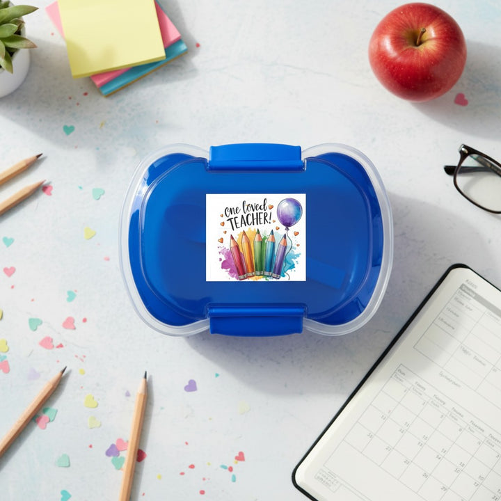 Sea Dragon Dreams two-tier blue bento box with One Loved Teacher pencil illustration on a desk with school supplies