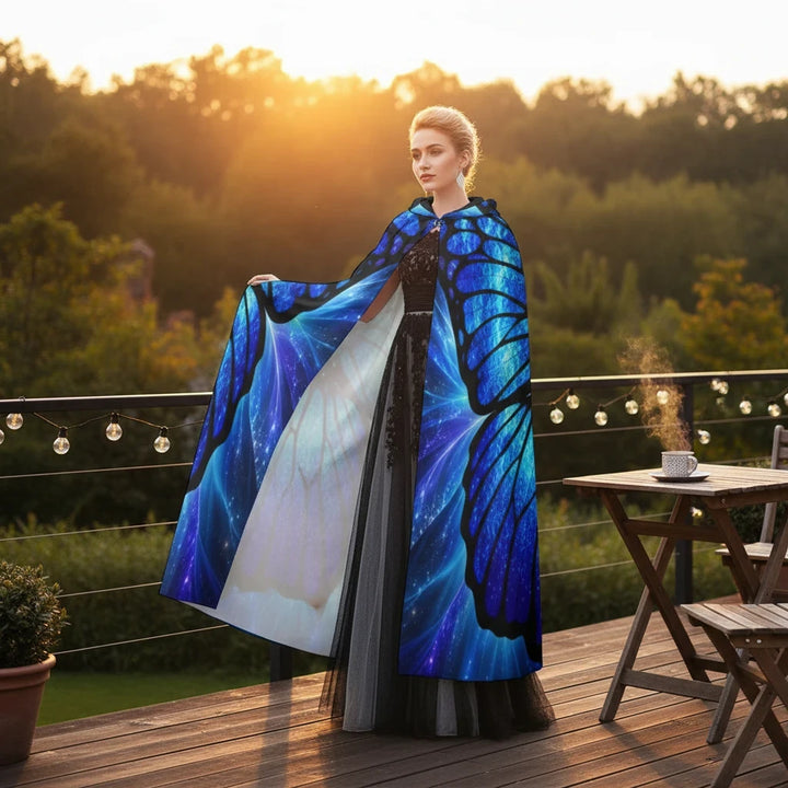 Sea Dragon Dreams hooded cloak with vibrant blue and black butterfly wing print worn by a woman on a sunset terrace.