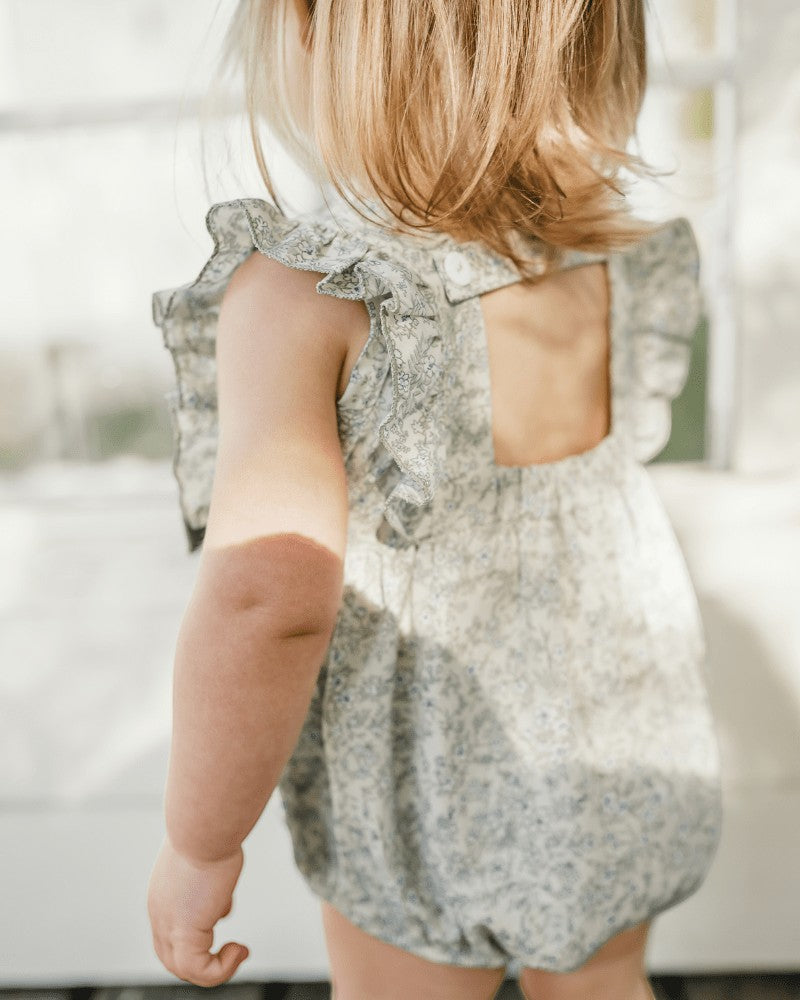 Sea Dragon Dreams bubble romper in blue floral print with ruffled sleeves and open back detail on a toddler