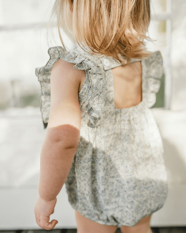Sea Dragon Dreams bubble romper in blue floral print with ruffled sleeves and open back detail on a toddler