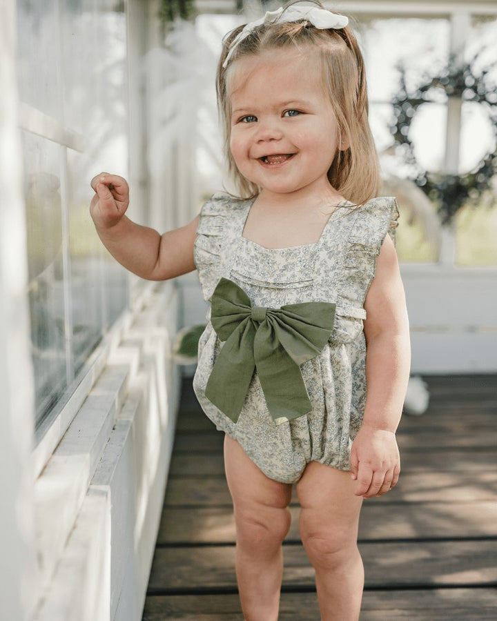 Toddler girl wearing Sea Dragon Dreams blue floral bubble romper with a large olive green bow front detail