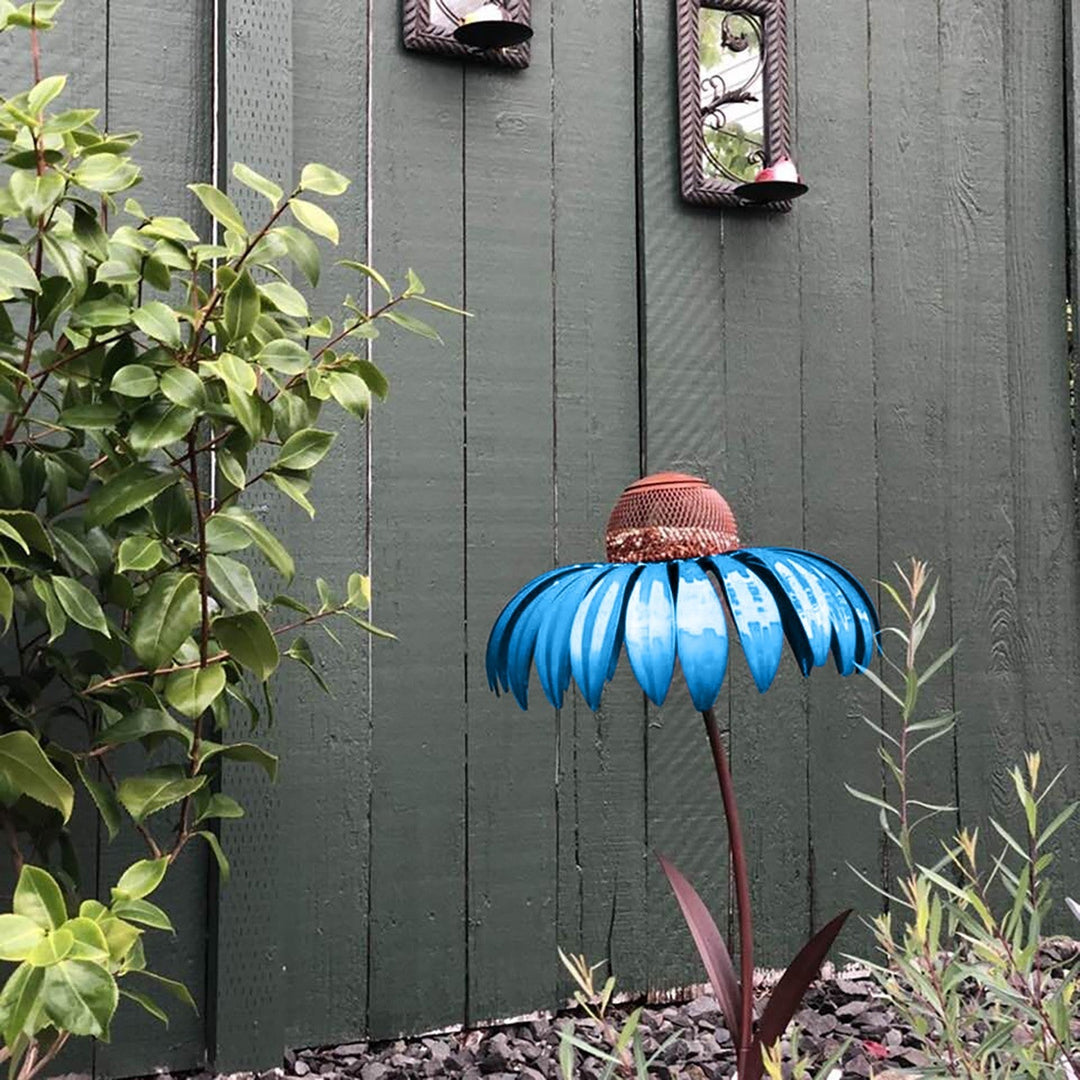 Sea Dragon Dreams blue metal petal-shaped bird feeder standing in a garden against a dark green wooden fence.