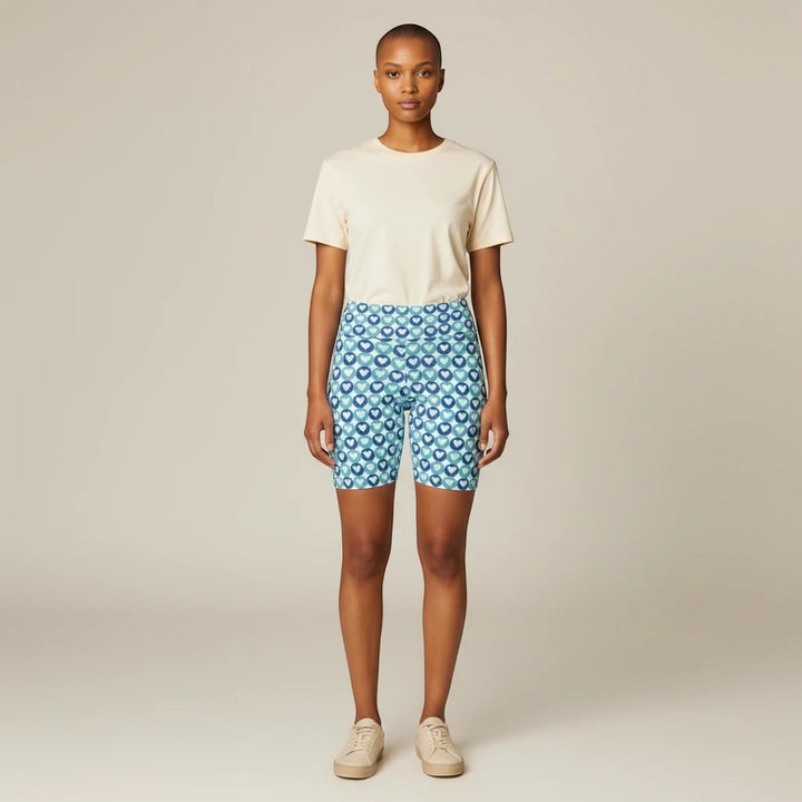 Model wearing Sea Dragon Dreams blue heart pattern polyester workout shorts with a neutral t-shirt and sneakers.