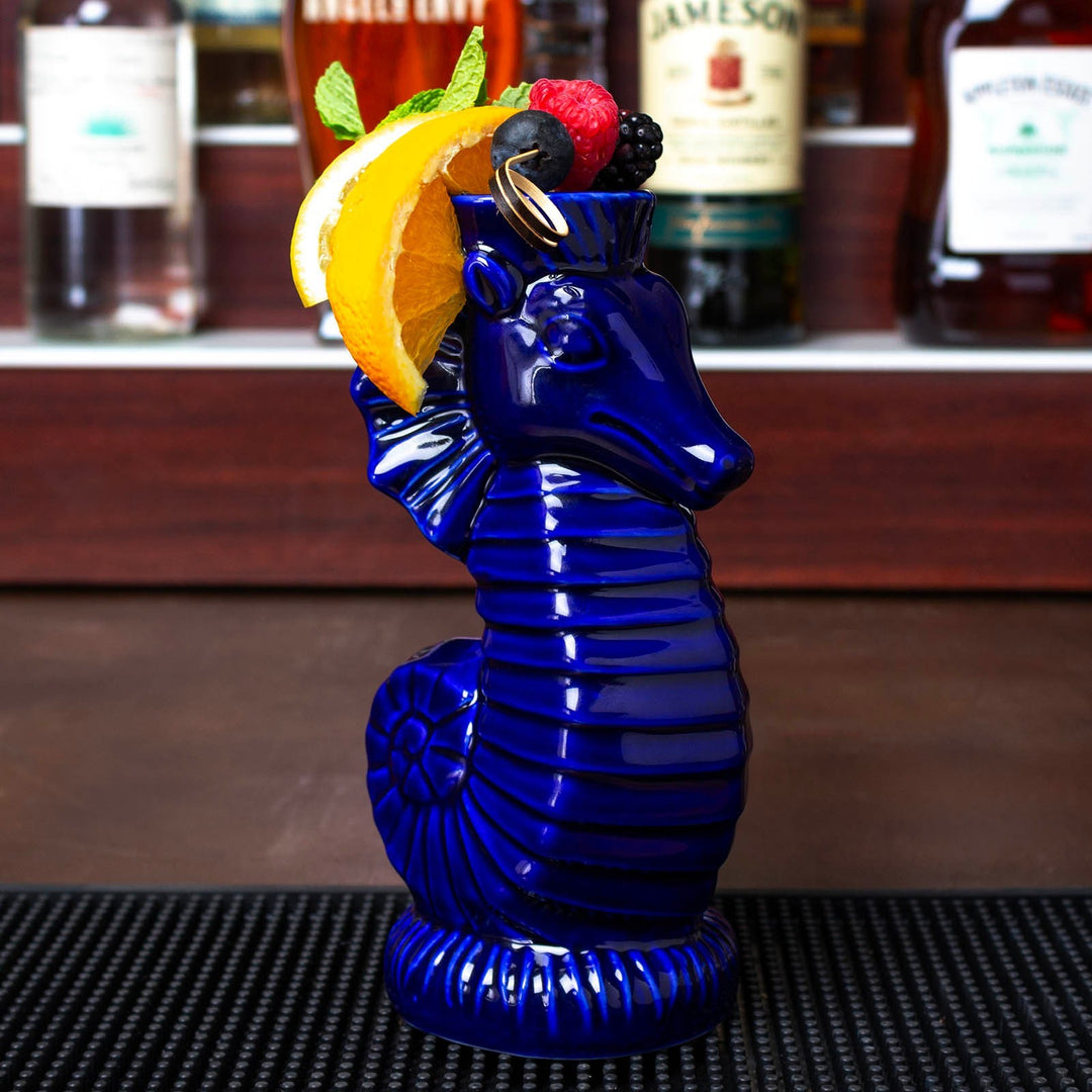 Sea Dragon Dreams ceramic seahorse tiki mug in deep blue glaze, garnished with fresh fruit on a bar mat.