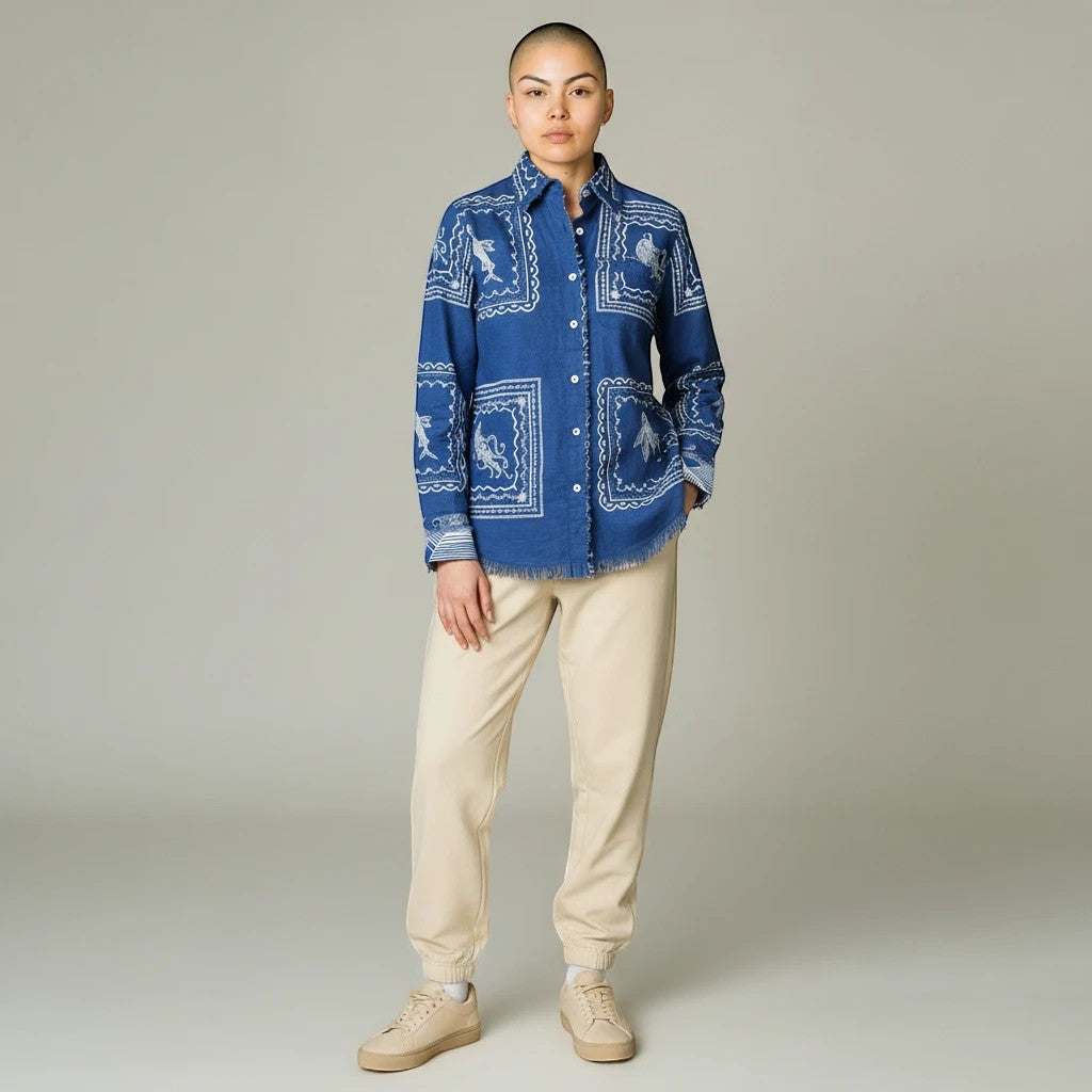 Model wearing a Sea Dragon Dreams blue denim blouse with white sea life print and frayed hem, paired with beige joggers.