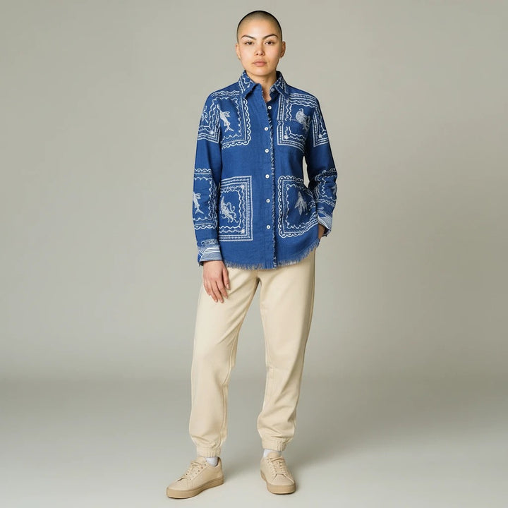 Model wearing a Sea Dragon Dreams blue denim blouse with white sea life print and frayed hem, paired with beige joggers.