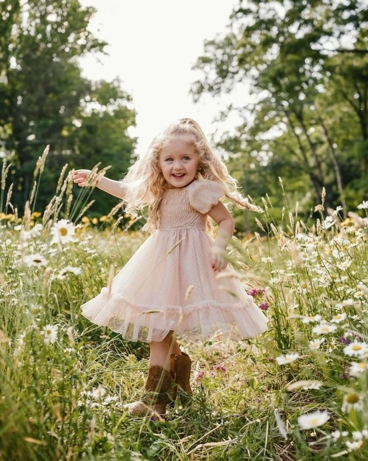Sea Dragon Dreams toddler girl wearing a blush tulle party dress with puff sleeves in a sunny wildflower meadow.