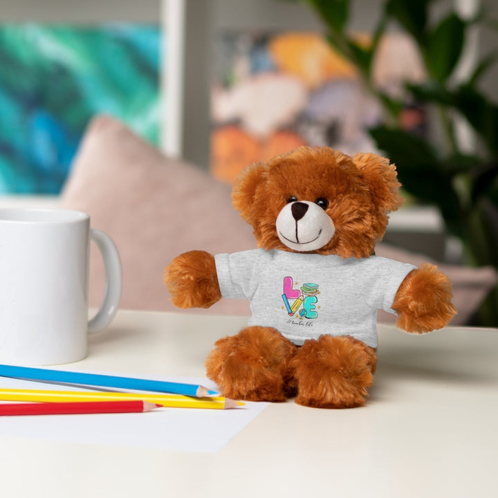 Sea Dragon Dreams brown plush bear wearing a grey t-shirt with Love Teacher Life text on a desk with pencils.