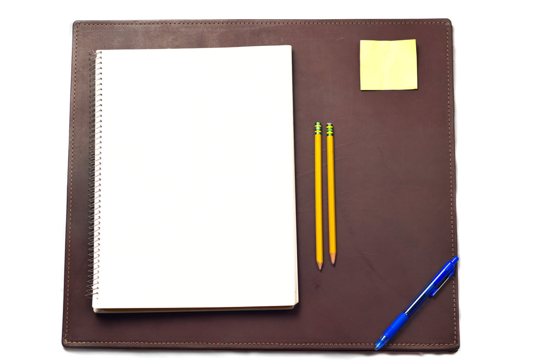 Sea Dragon Dreams brown top-grain leather desk pad with a notebook, two pencils, a pen, and a sticky note on top.