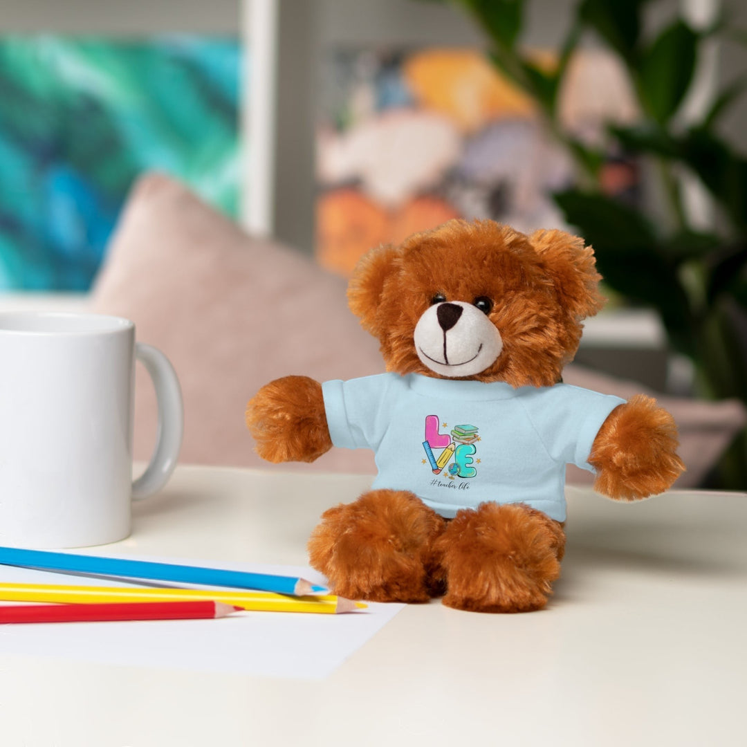 Sea Dragon Dreams brown plush teddy bear wearing a light blue t-shirt with Love Teacher Life graphic on a desk