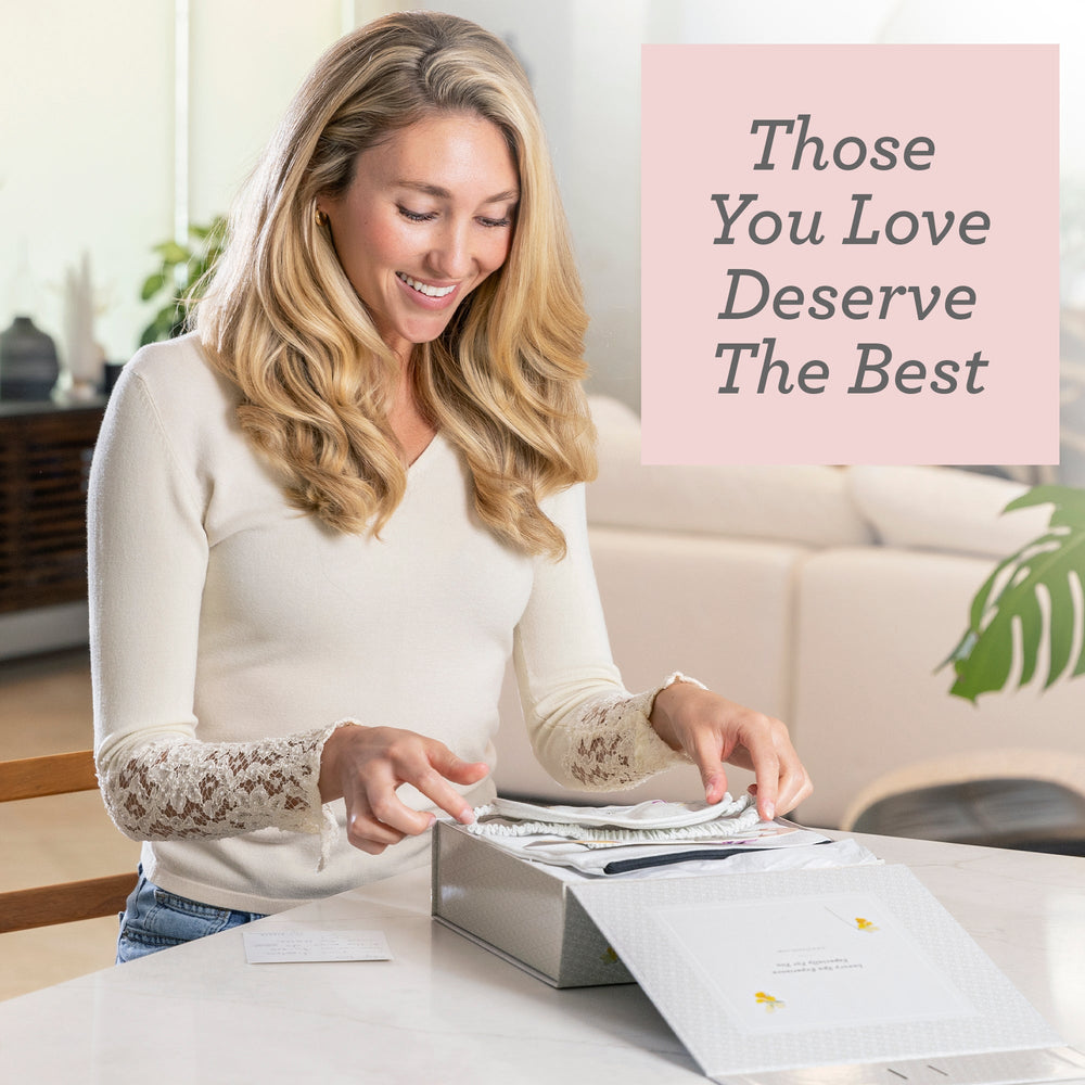 A woman smiling while opening a Sea Dragon Dreams CBD lavender bath bomb gift set at a table.