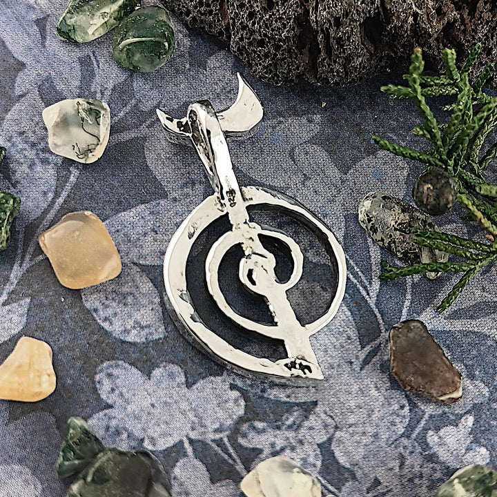 Sea Dragon Dreams handmade sterling silver Cho Ku Rei Reiki pendant with a polished spiral symbol on a floral fabric