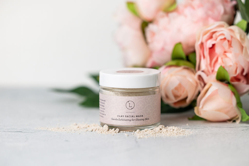 Sea Dragon Dreams clay facial mask in a glass jar, surrounded by soft pink peonies for a spa-inspired aesthetic.