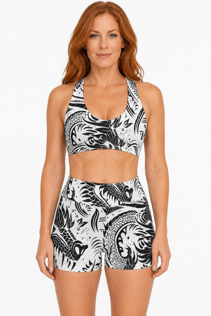 A woman wearing a Sea Dragon Dreams black and white dragon print sports bra and high-waisted shorts activewear set.