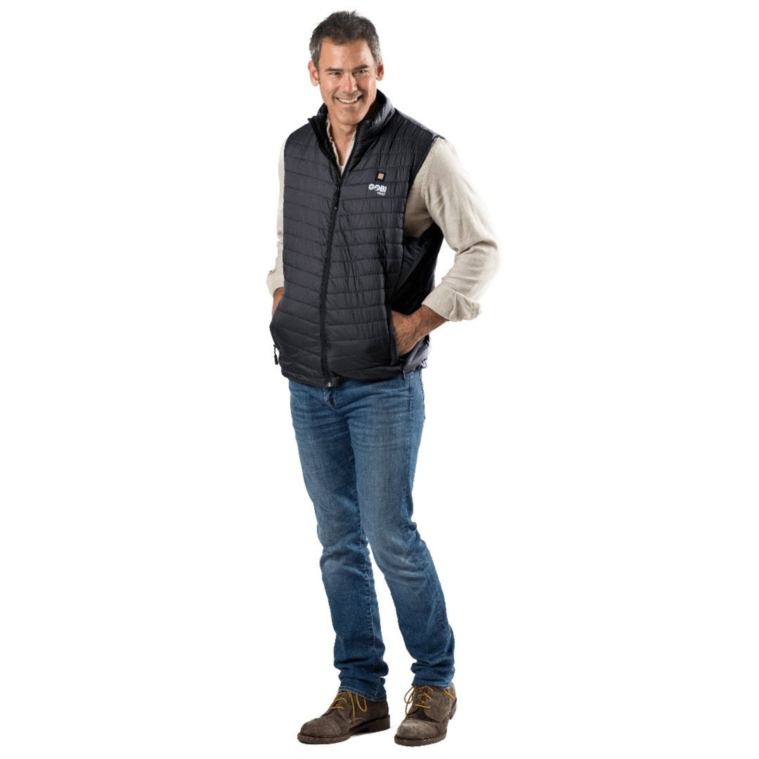 A man wearing a Sea Dragon Dreams black Dune heated vest over a beige shirt and blue jeans, standing against a white background.