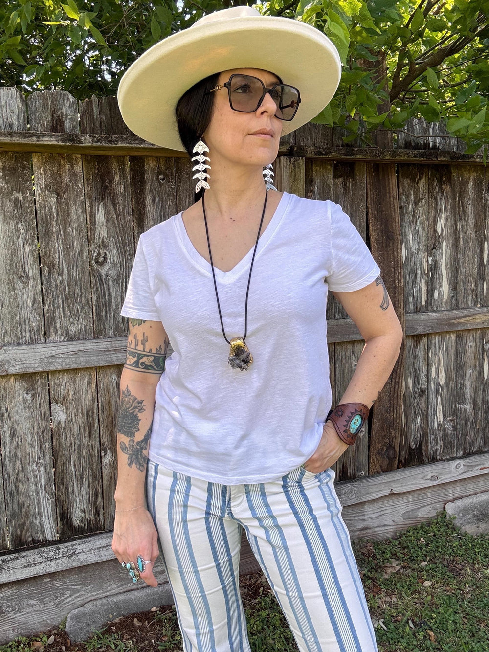 Sea Dragon Dreams handmade silver-tone fish bone earrings with floral cutouts worn by a woman in a white hat