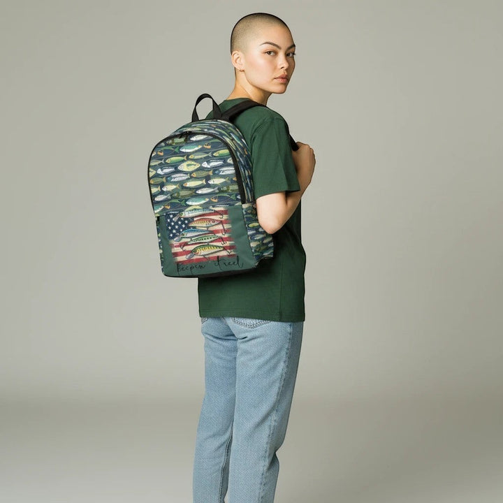 Model wearing a Sea Dragon Dreams unisex nylon backpack with a fish line pattern and American flag fishing graphic.