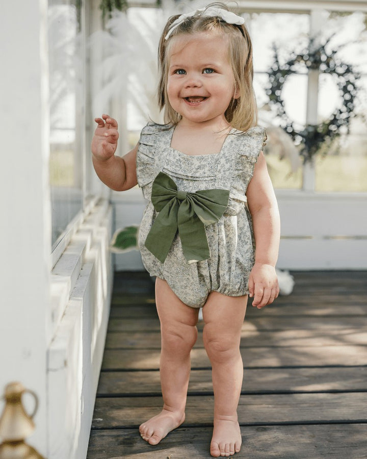 Sea Dragon Dreams baby girl wearing a blue floral bubble romper with a large green bow front detail