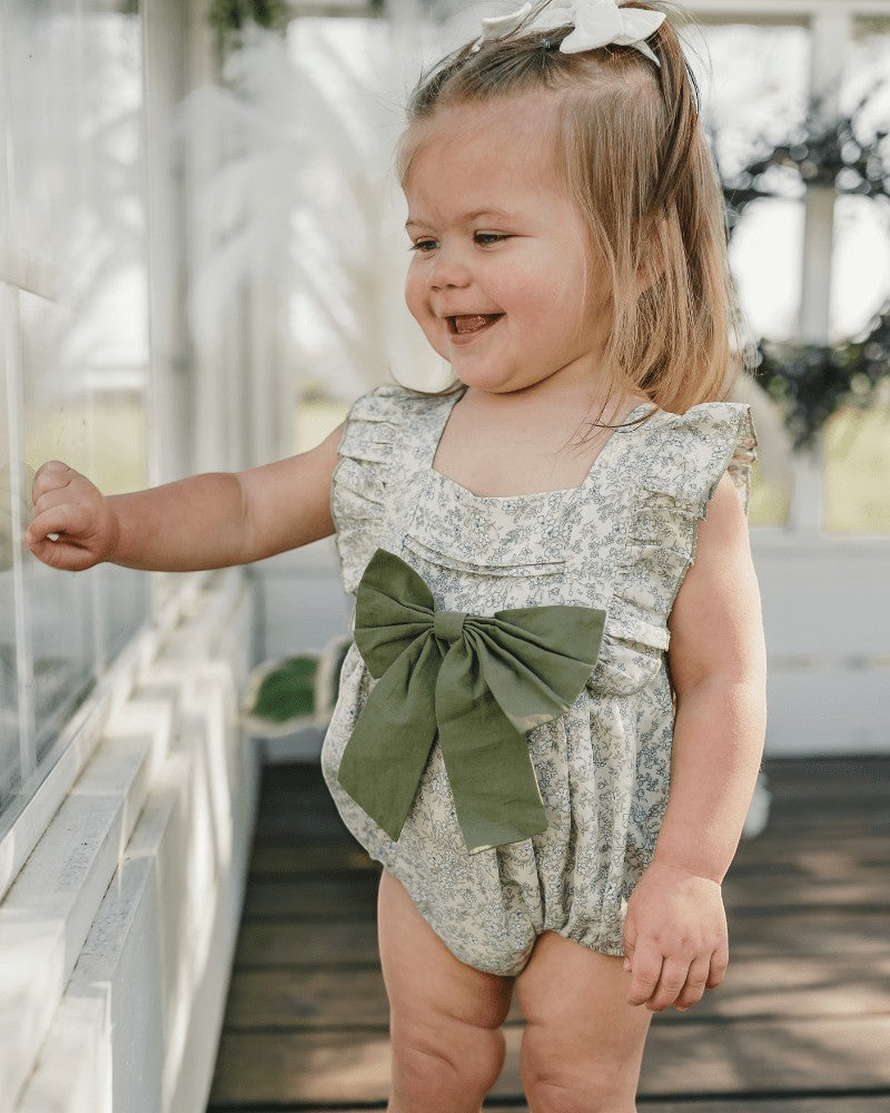 Sea Dragon Dreams toddler girl wearing a blue floral bubble romper with a large olive green bow front detail