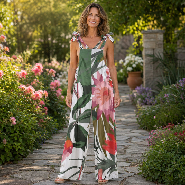 Sea Dragon Dreams floral print jersey jumpsuit with tie-shoulder straps worn by a smiling woman in a garden setting.