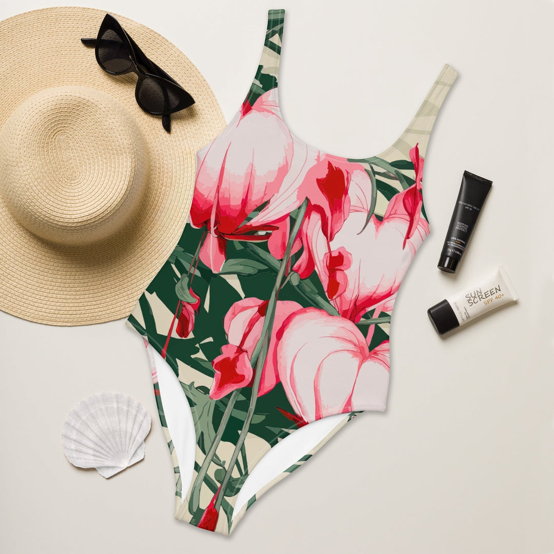 Sea Dragon Dreams floral one-piece swimsuit with scoop neckline, laid flat with a straw hat and sunscreen.