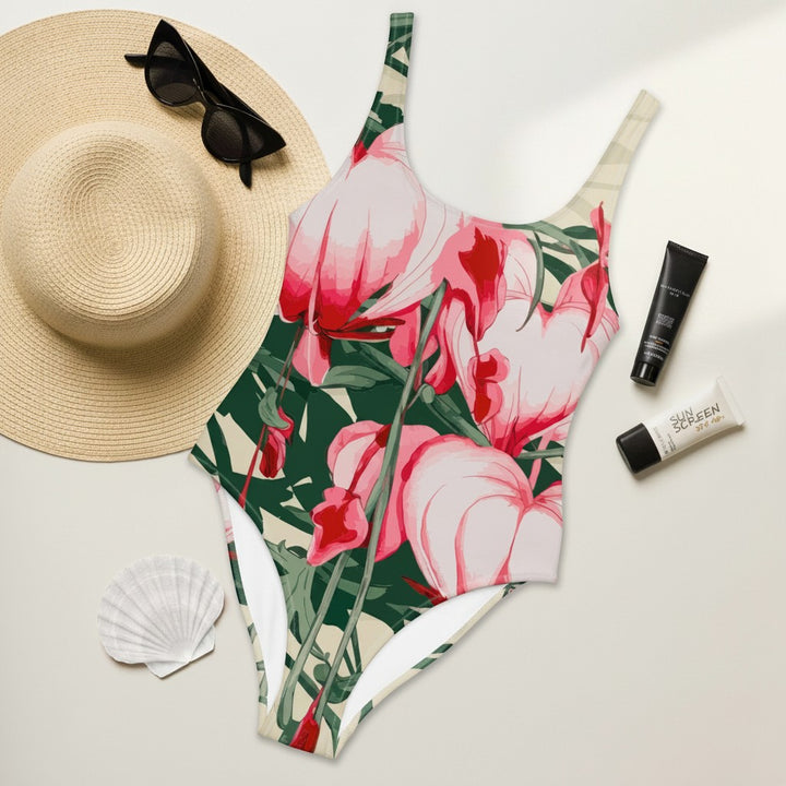 Sea Dragon Dreams floral print one-piece swimsuit with scoop neckline, laid flat with a sun hat and sunscreen.