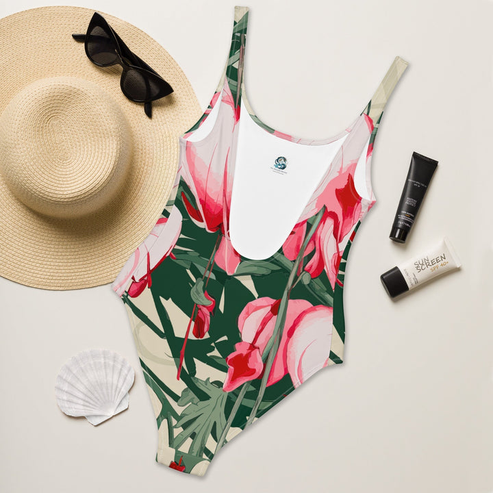 Sea Dragon Dreams floral print one-piece swimsuit with scoop back, styled with a straw hat and sunscreen.