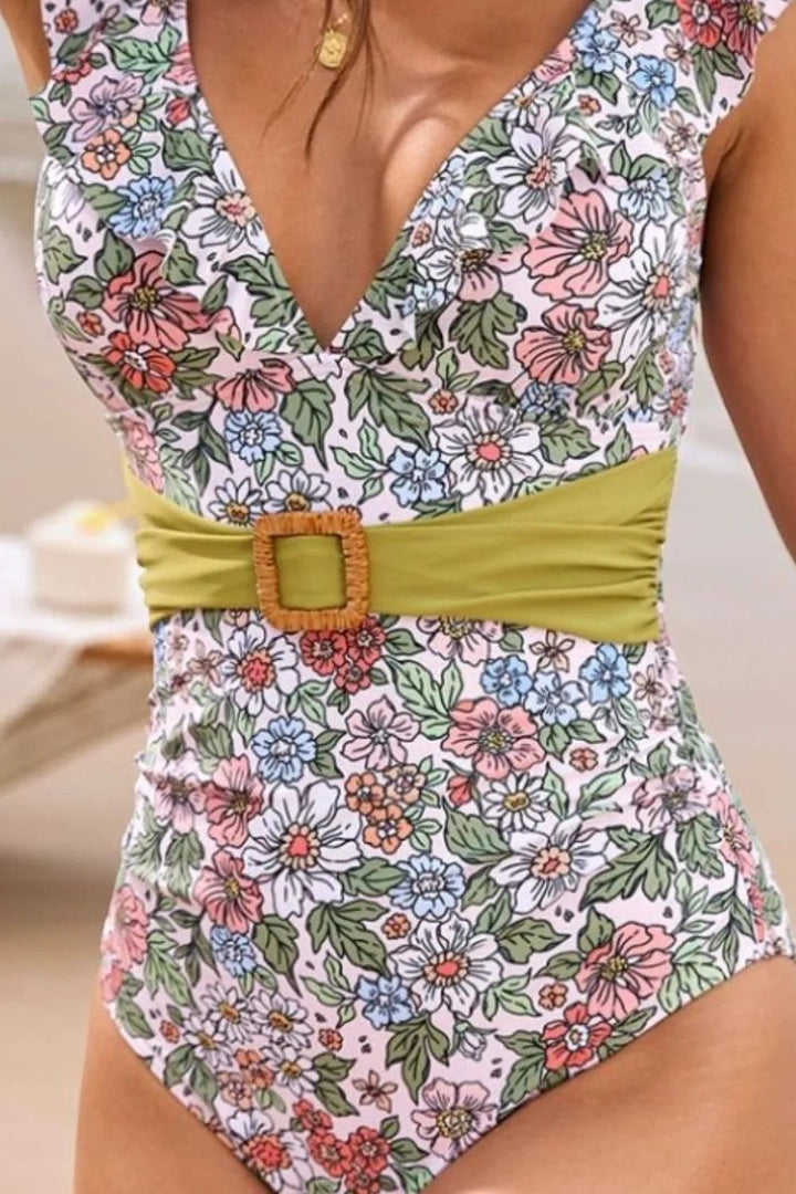 Sea Dragon Dreams floral one-piece swimsuit with a plunging V-neck, ruffle trim, and a green belted waist detail.