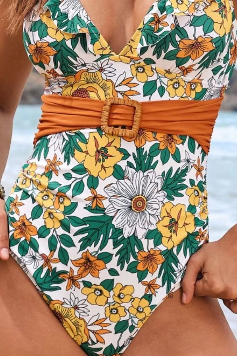 Sea Dragon Dreams one-piece swimsuit with a white floral print, deep V-neck, ruffle trim, and a tan belted waist.