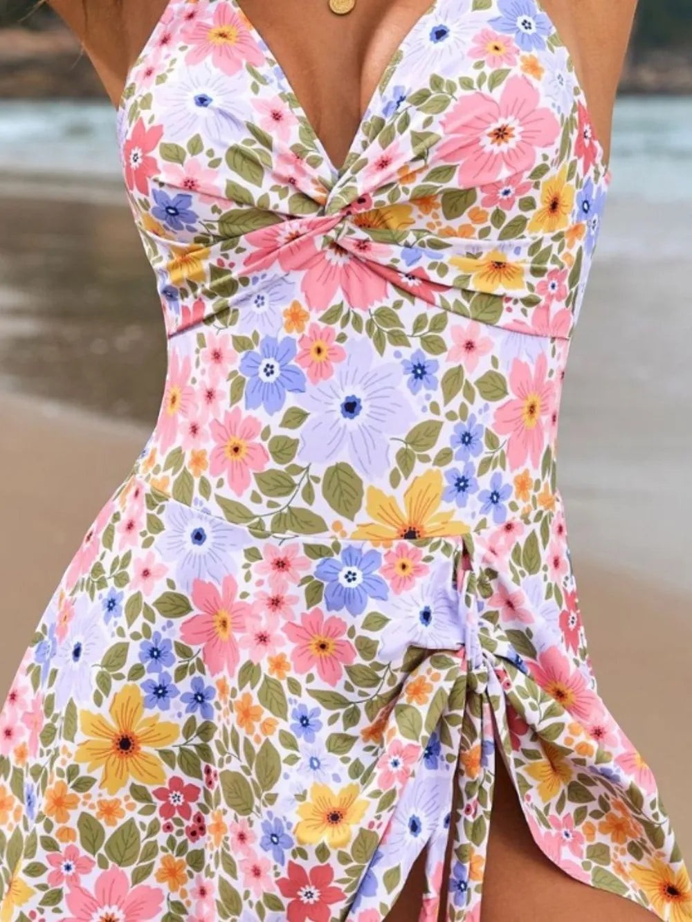 Sea Dragon Dreams floral one-piece swimsuit with a twisted front and double spaghetti straps on a beach background.