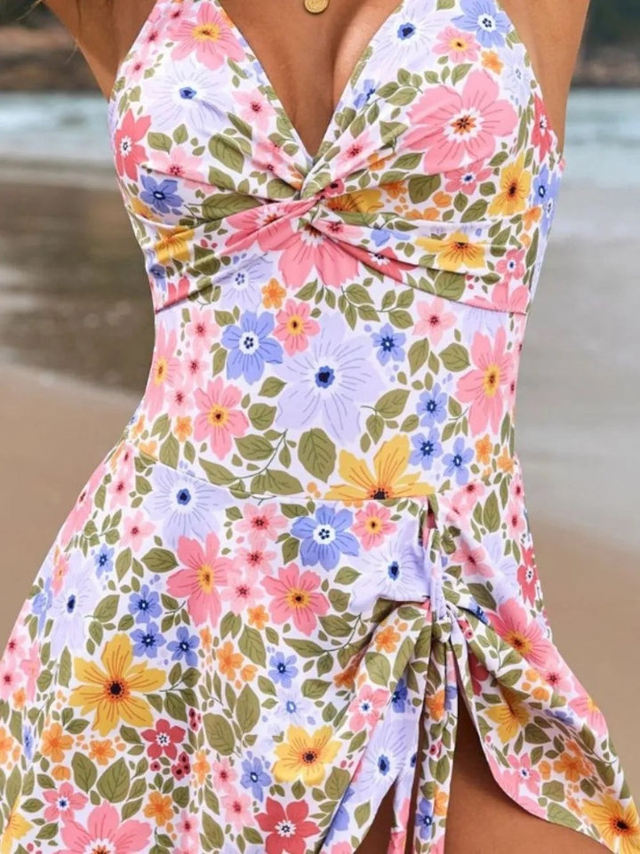 Sea Dragon Dreams floral one-piece swimsuit with a twisted front and double spaghetti straps on a beach background.