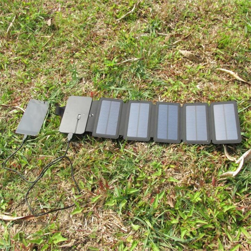 Sea Dragon Dreams portable folding solar panel charger charging a smartphone on a grassy field