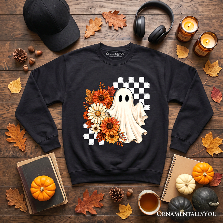 Sea Dragon Dreams black sweatshirt featuring a ghost, orange flowers, and checkered pattern on a rustic autumn desk.